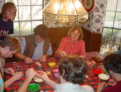 people sitting at a checkered kitchen table, with cups of colored icing, decorating cookies